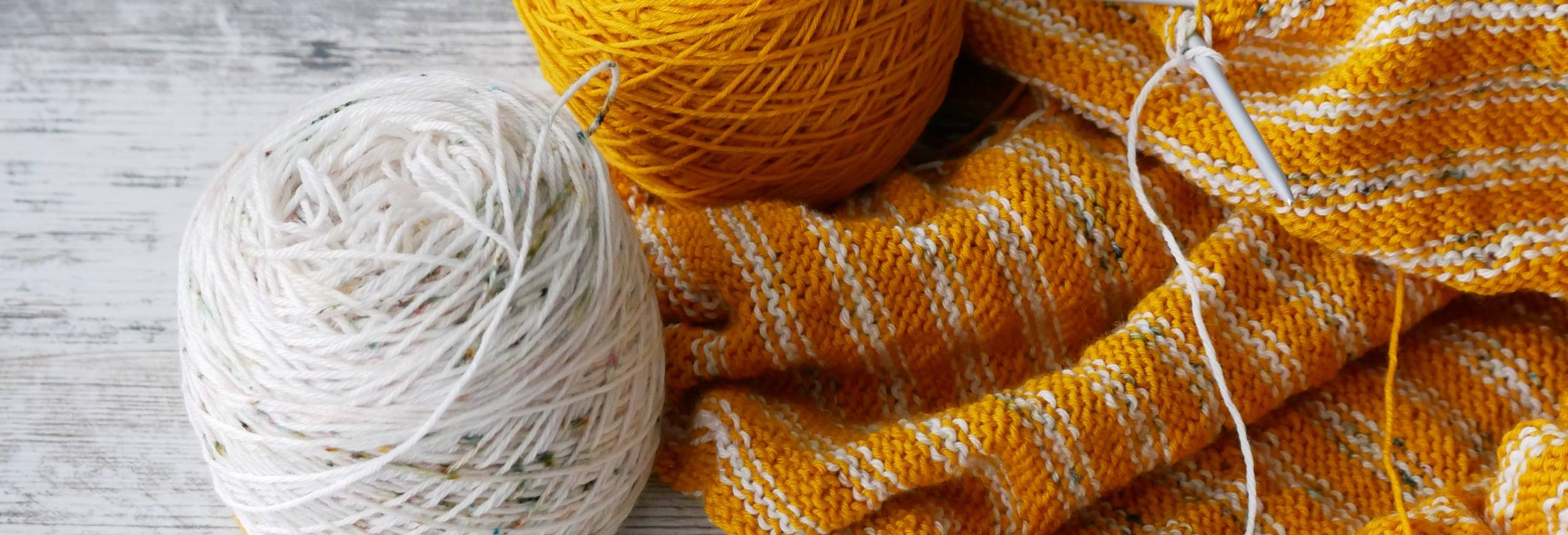 Golden Yellow and White Speckled yarn sits next to a striped knitting project